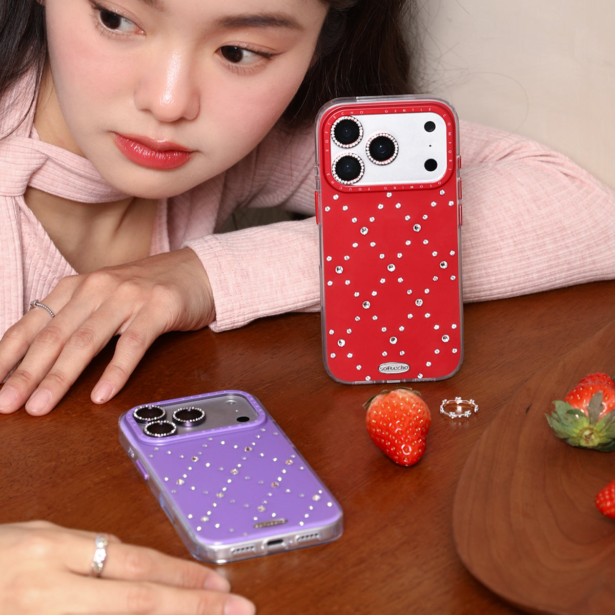 Two phone cases, one red with white polka dots and one purple, on a wooden surface with a person partially visible.
