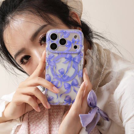 Person holding a phone with a purple floral case, wearing a white sweater and a headband with a purple bow.