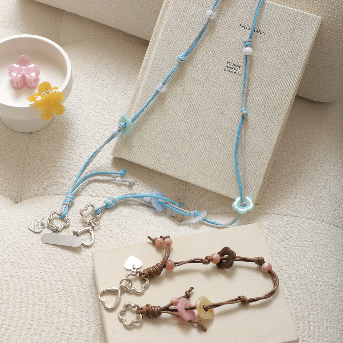 Two necklaces with floral and heart charms on a textured surface with a book and small decorative items.