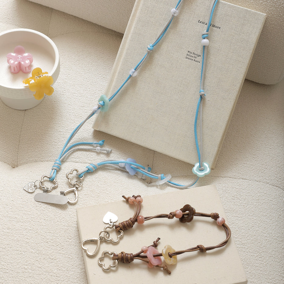 Two necklaces with floral and heart charms on a textured surface with a book and small decorative items.