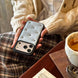 Person holding a phone with a decorative case, sitting at a table with a cup of coffee.