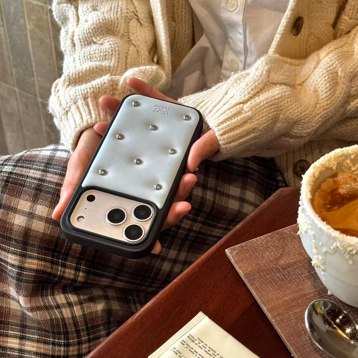Person holding a phone with a decorative case, sitting at a table with a cup of coffee.