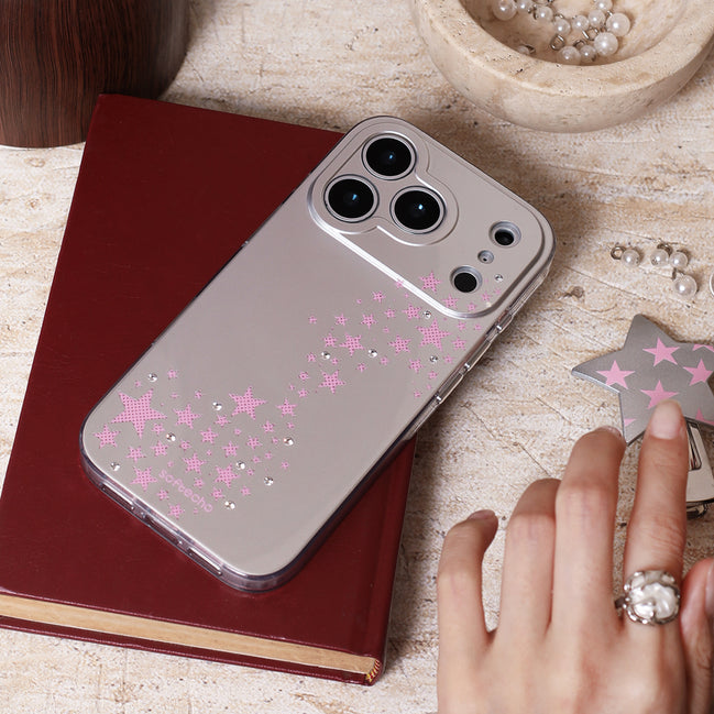 Phone case with pink star designs on a wooden surface with a hand and jewelry.