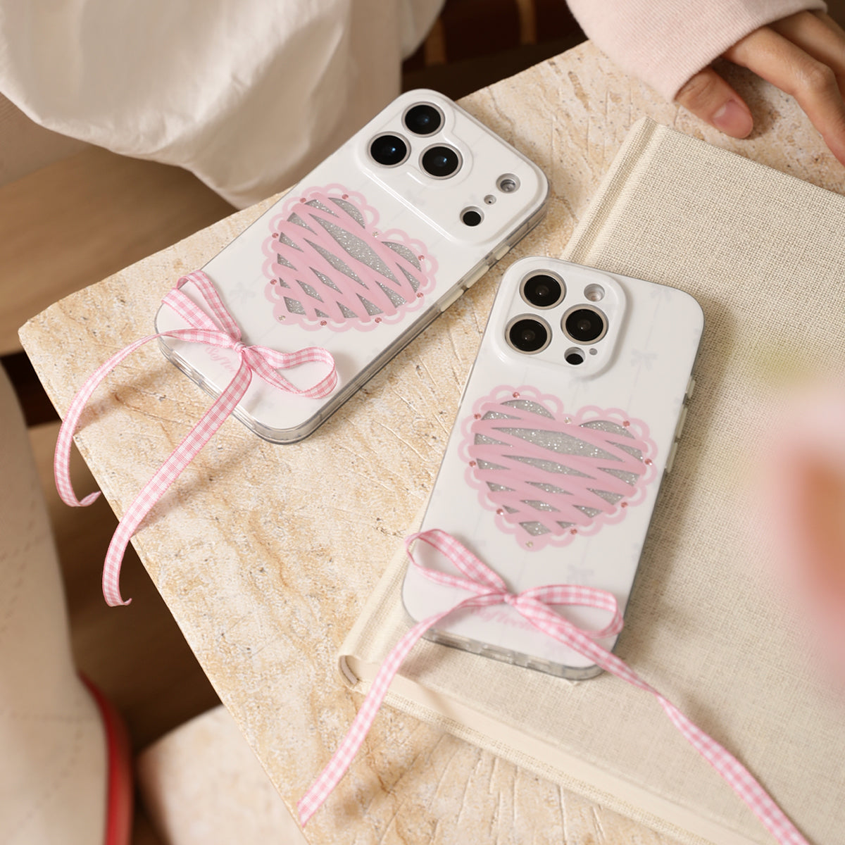 Two phone cases with heart designs and pink ribbons on a stone surface.