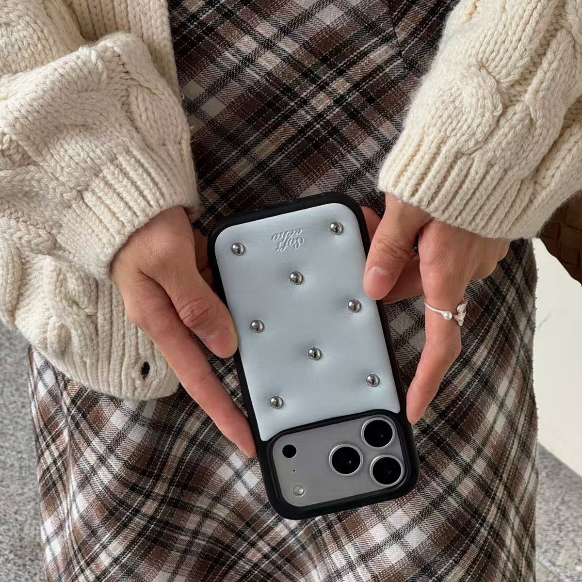 Person holding a phone with a decorative case featuring studs