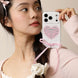 Woman holding a phone with a heart-shaped case and pink ribbon