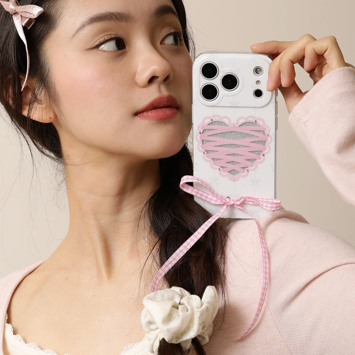 Woman holding a phone with a heart-shaped case and pink ribbon