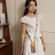 Woman wearing a white dress with a phone case hanging from her strap in an indoor setting.