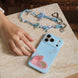 Blue phone case with a pink heart design on a wooden surface, next to a hand and a necklace.