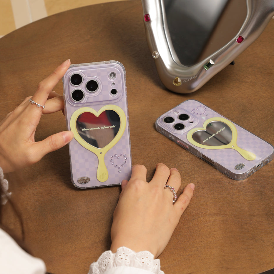 Two phone cases with heart mirror designs on a wooden table.