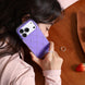 Person holding a purple phone case with rhinestones on a wooden surface.