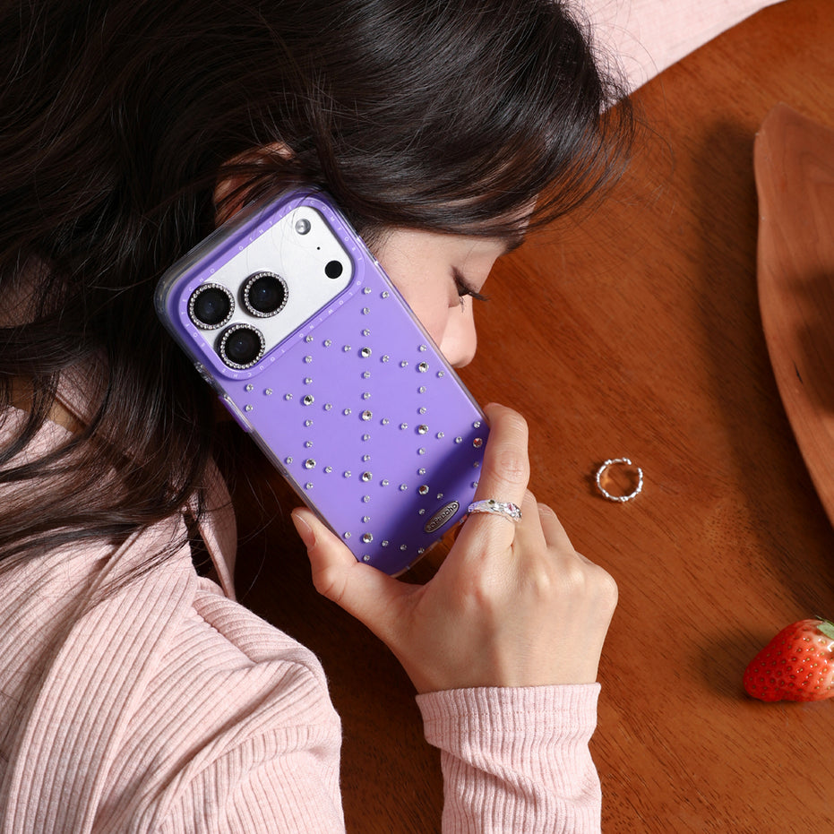 Person holding a purple phone case with rhinestones on a wooden surface.
