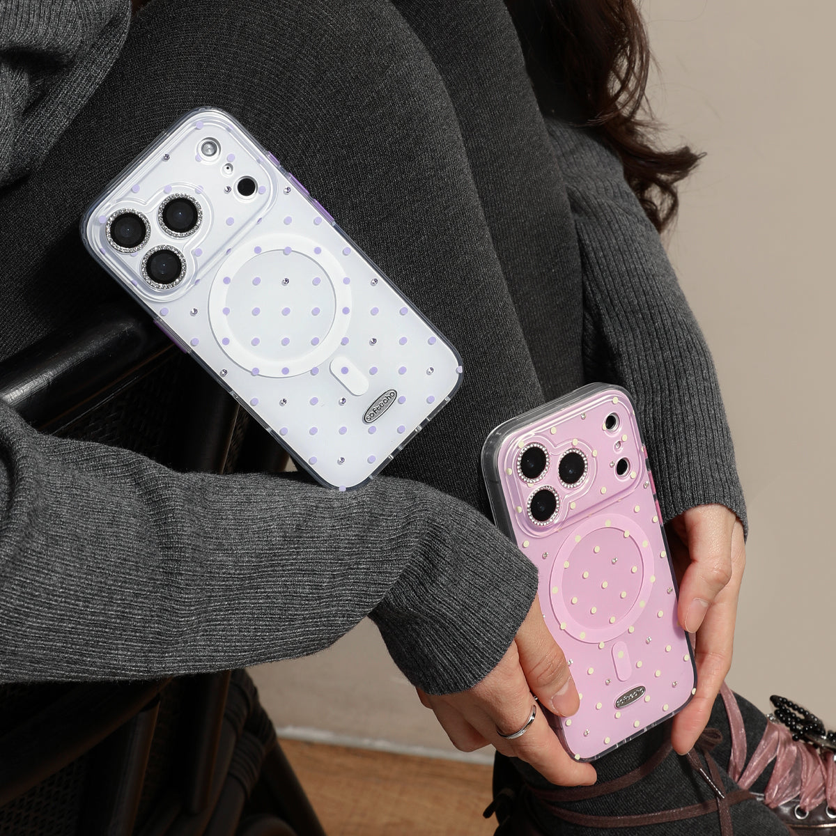 Two phone cases, one white and one pink, held by a person wearing a gray sweater.