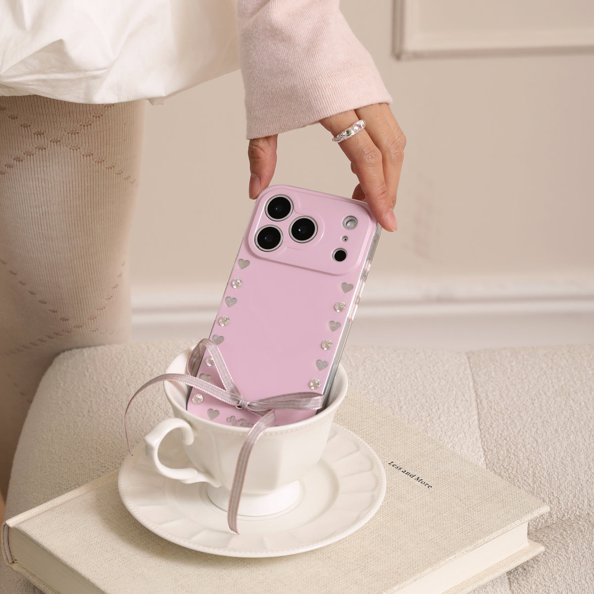 Pink phone case with heart designs held over a white teacup on a saucer.