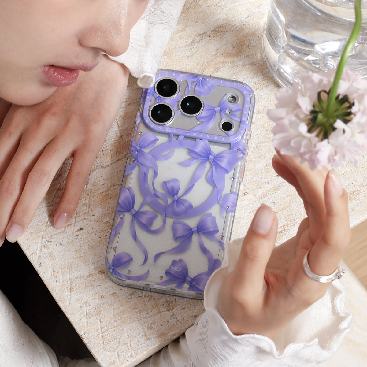 Person holding a phone with a purple floral case on a light surface.