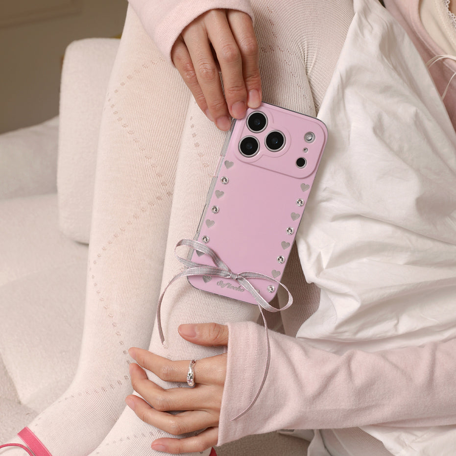 Person holding a pink phone case with heart designs and a bow.