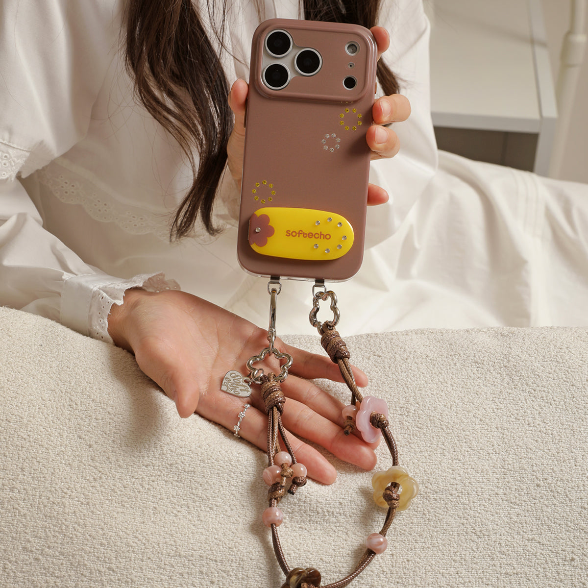 Person holding a phone with a decorative strap, wearing a white lace top.