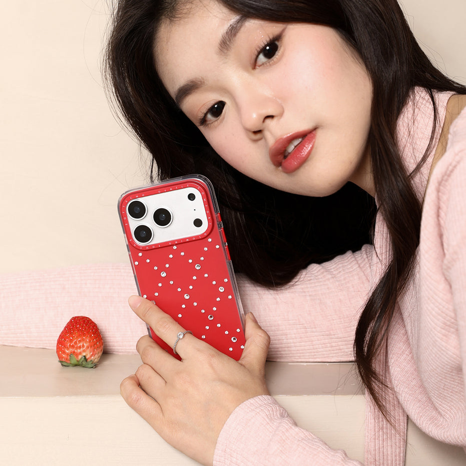 Woman holding a red phone case with rhinestones, next to a strawberry on a light background