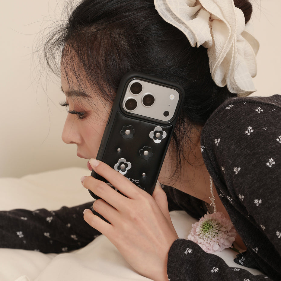 Woman holding a black phone case with floral designs, wearing a black top with white patterns.