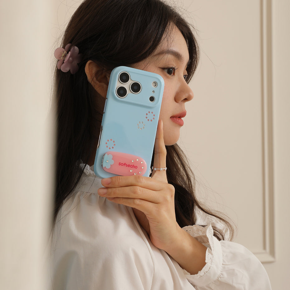 Woman holding a blue phone case with a pink heart design against a beige wall.