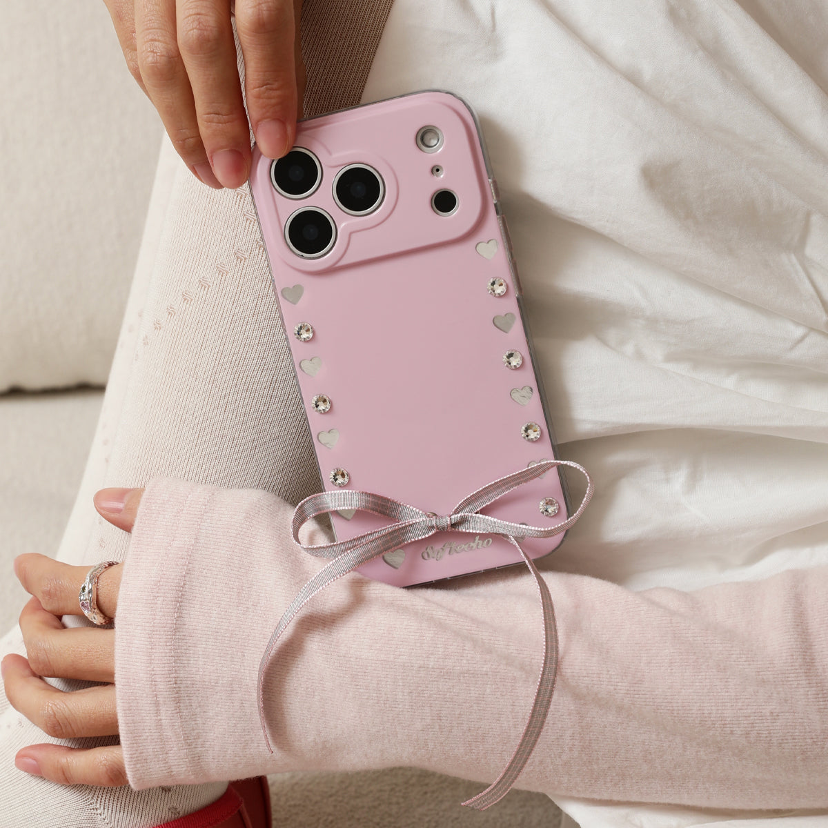Pink phone case with heart designs held by a person wearing a light pink sweater.