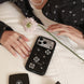 Person holding a black phone case with floral designs on a light surface.