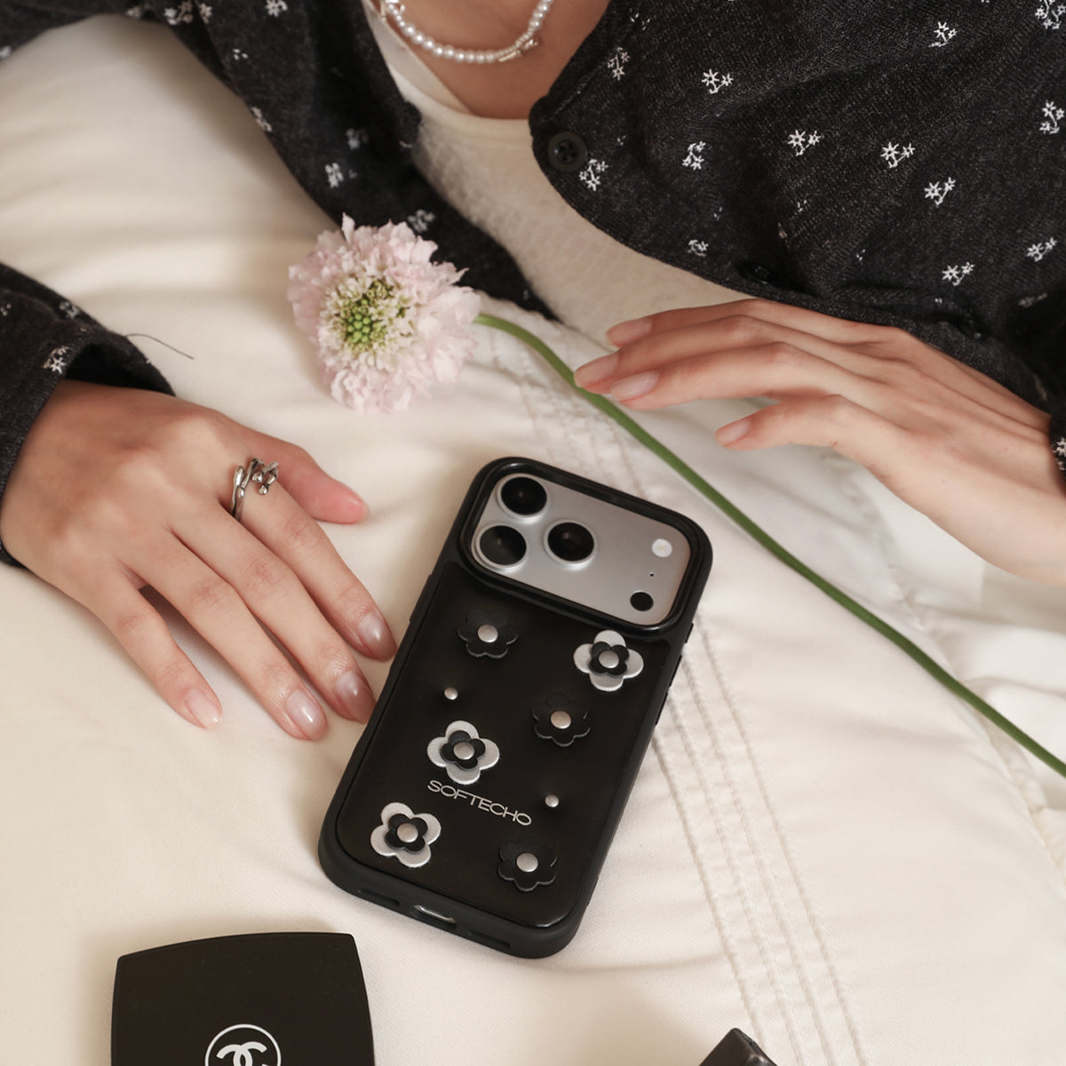 Person holding a black phone case with floral designs on a light surface.