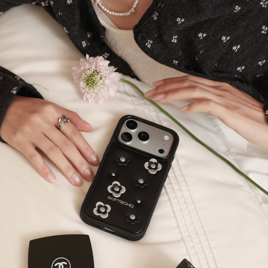 Person holding a black phone case with floral designs on a light surface.