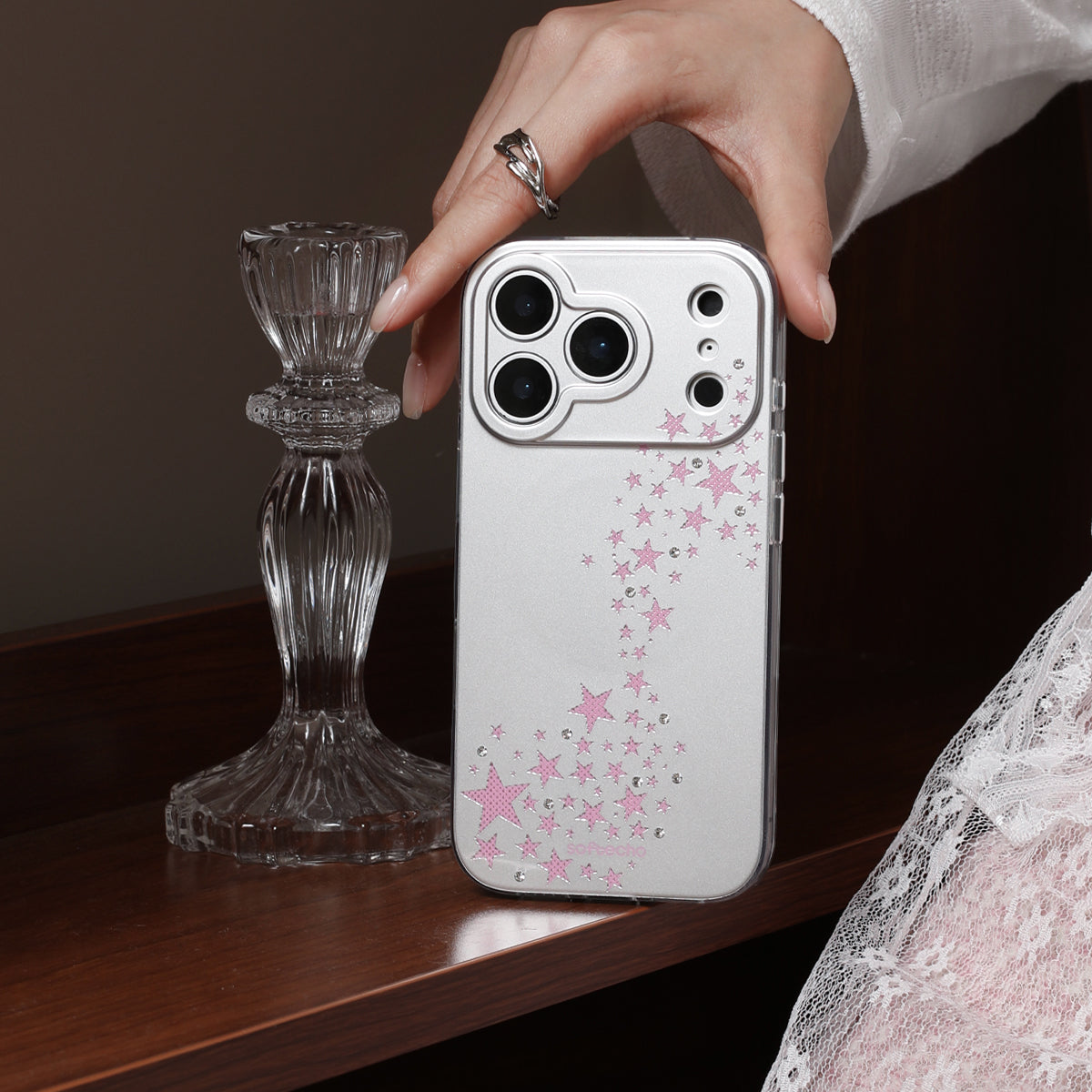 Person holding a phone with a star-patterned case next to a decorative glass candlestick.