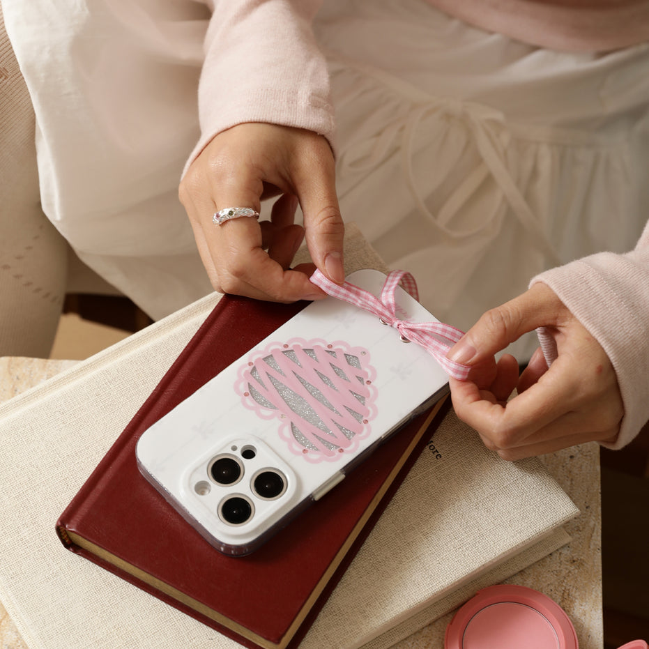 Person holding a phone with a pink heart design on a beige surface