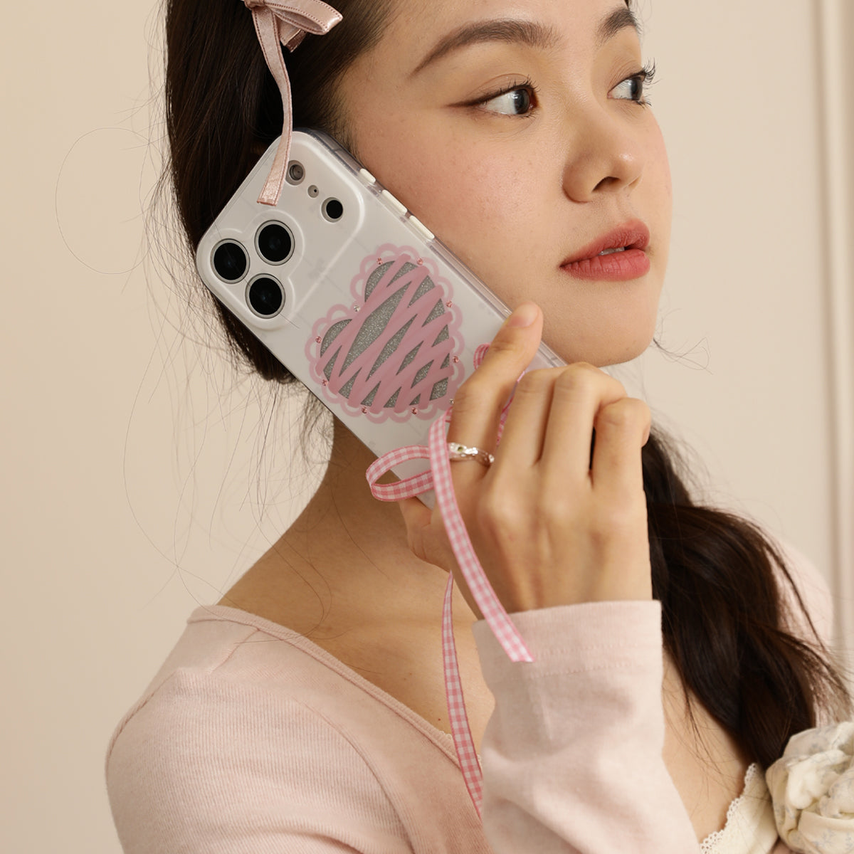 Woman holding a phone with a heart design and pink strap against a beige background