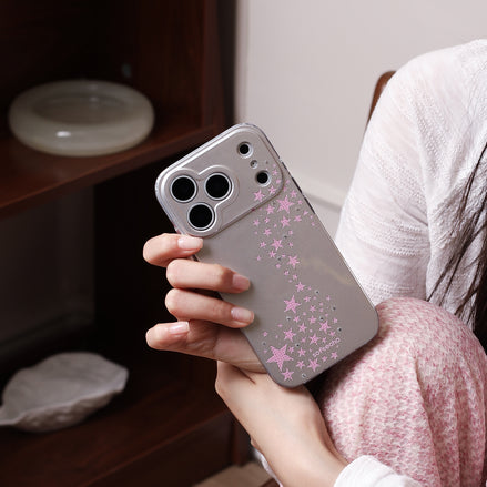 Person holding a phone with a pink star pattern case indoors.