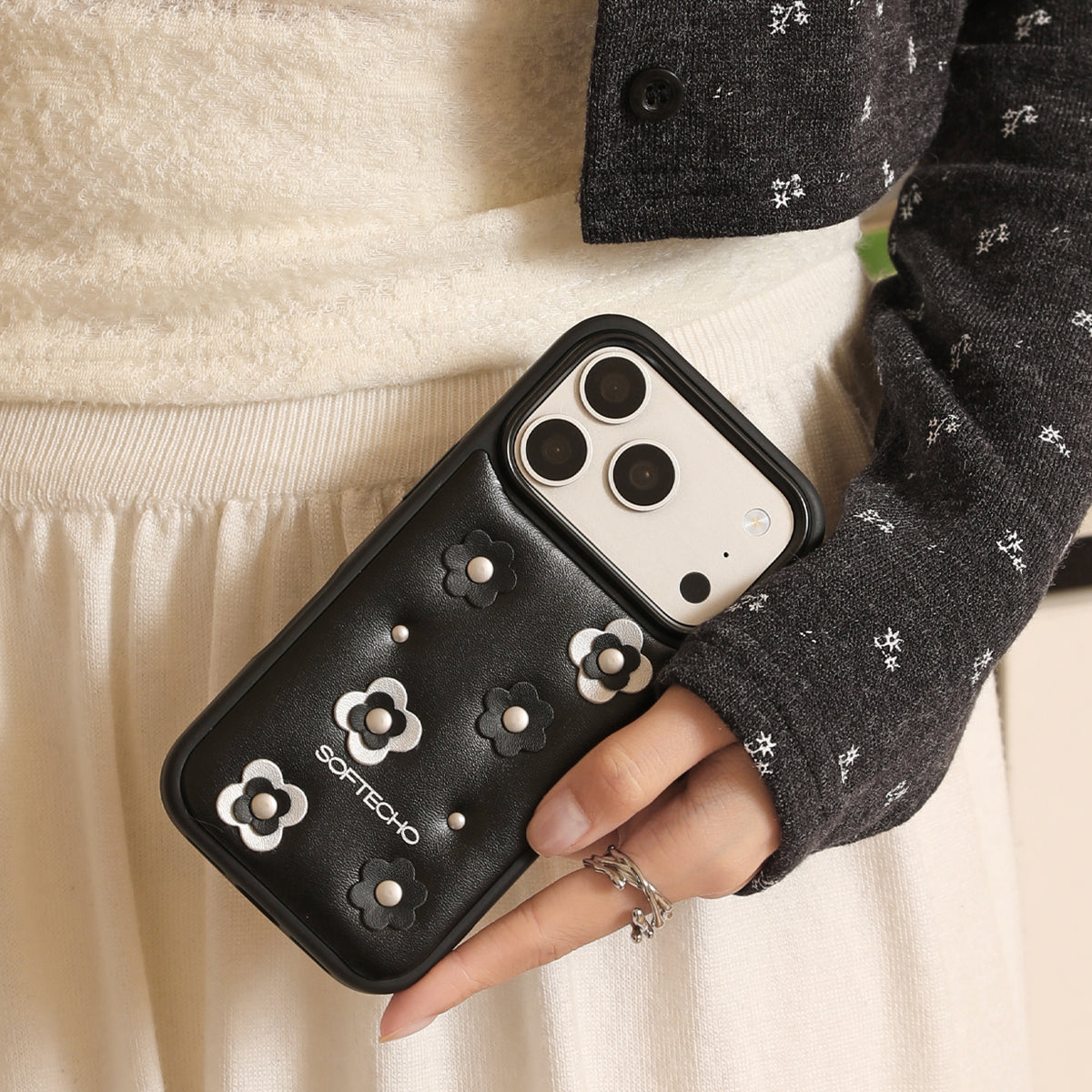 Person holding a black phone case with floral designs and 'softecho' branding.