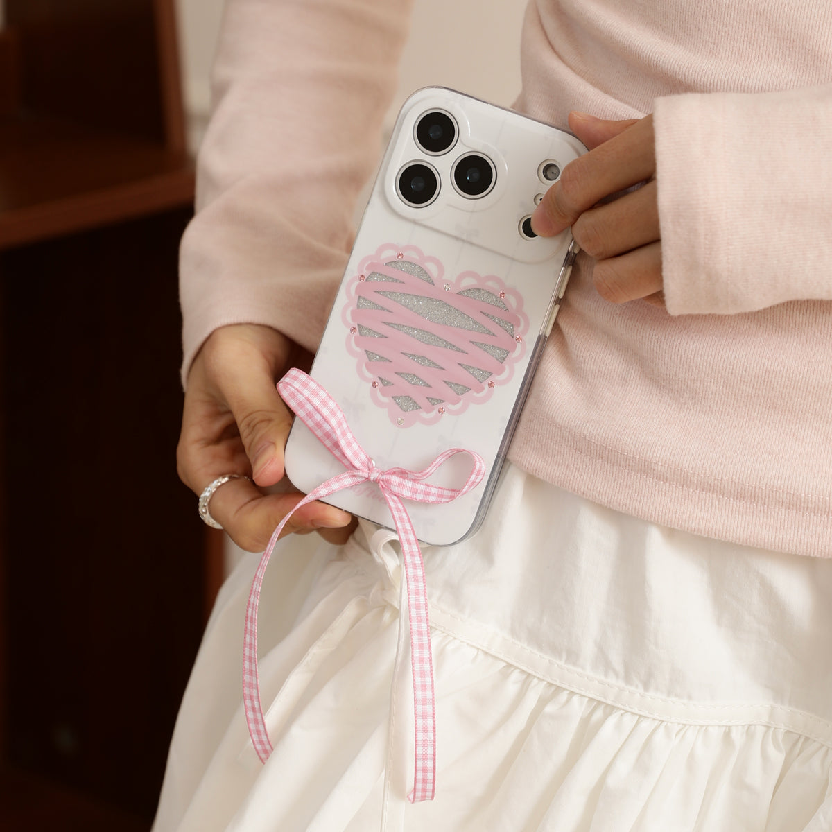 Person holding a phone with a heart design and pink ribbon, wearing a light pink sweater.