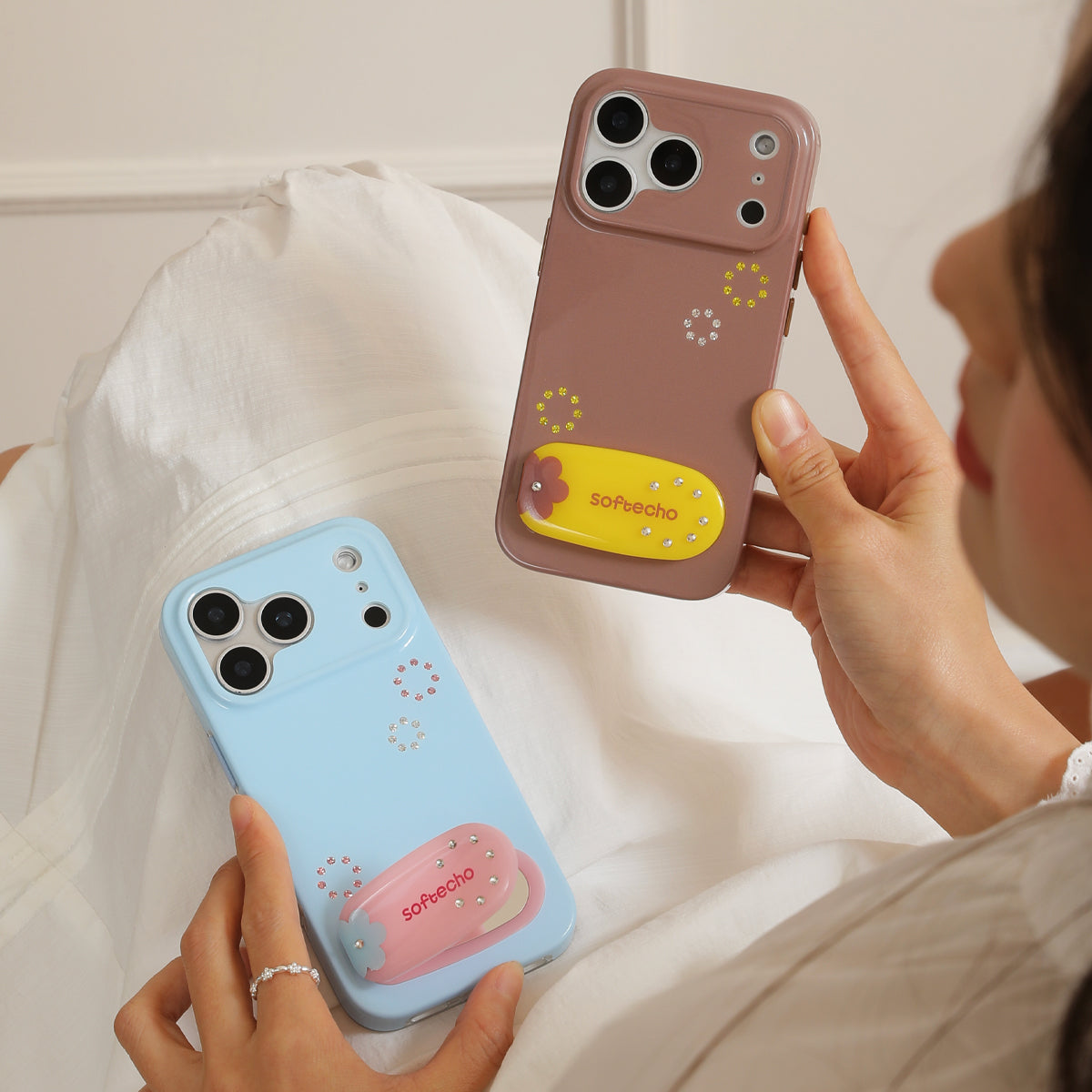 Two phone cases, one pink and one blue, held by a person against a white background.