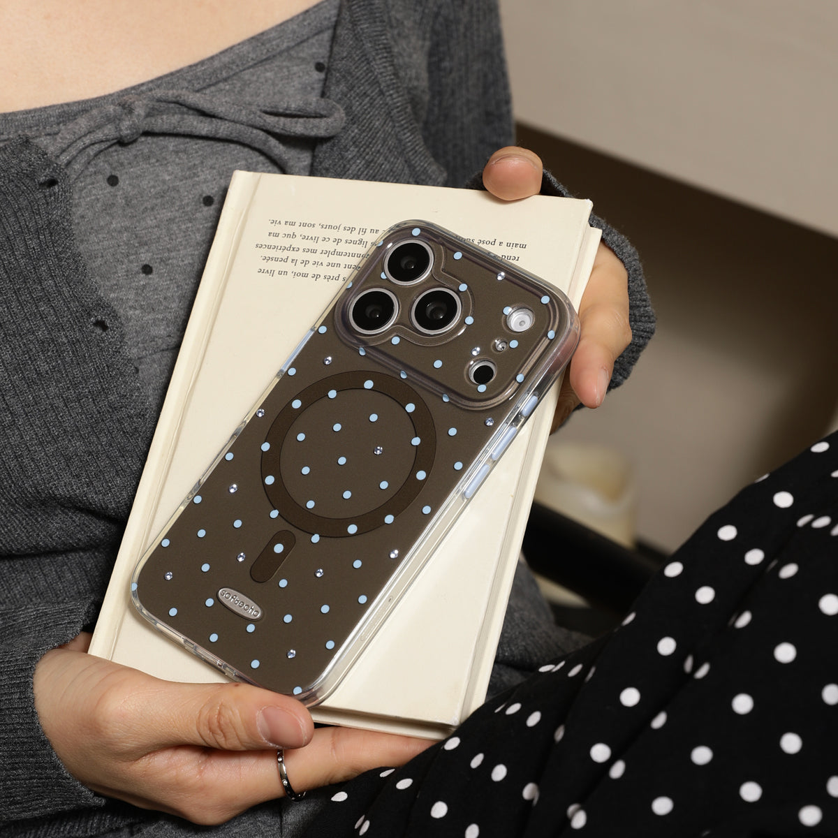 Person holding a phone with a polka dot case on a stack of books