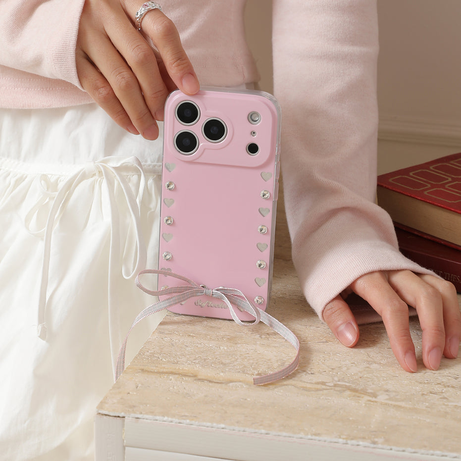 Pink phone case with decorative elements held by a person on a wooden surface.