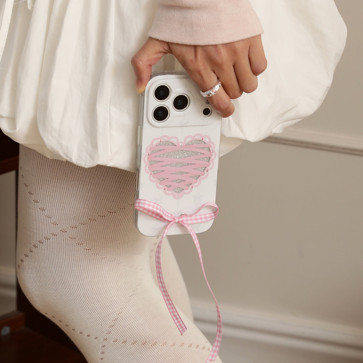 Phone case with heart design and pink ribbon held by a person wearing white pants.