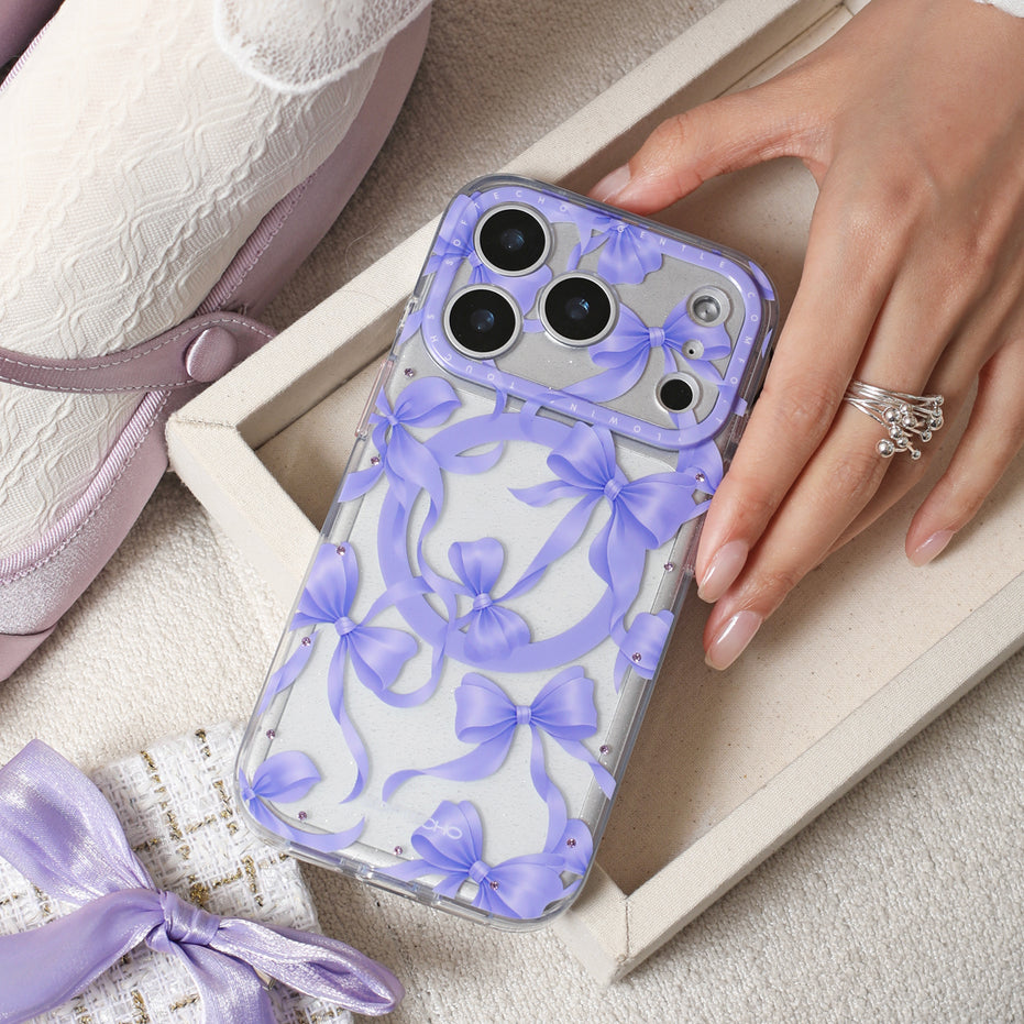 Phone case with purple bow pattern held by a hand, with a shoe and fabric in the background.