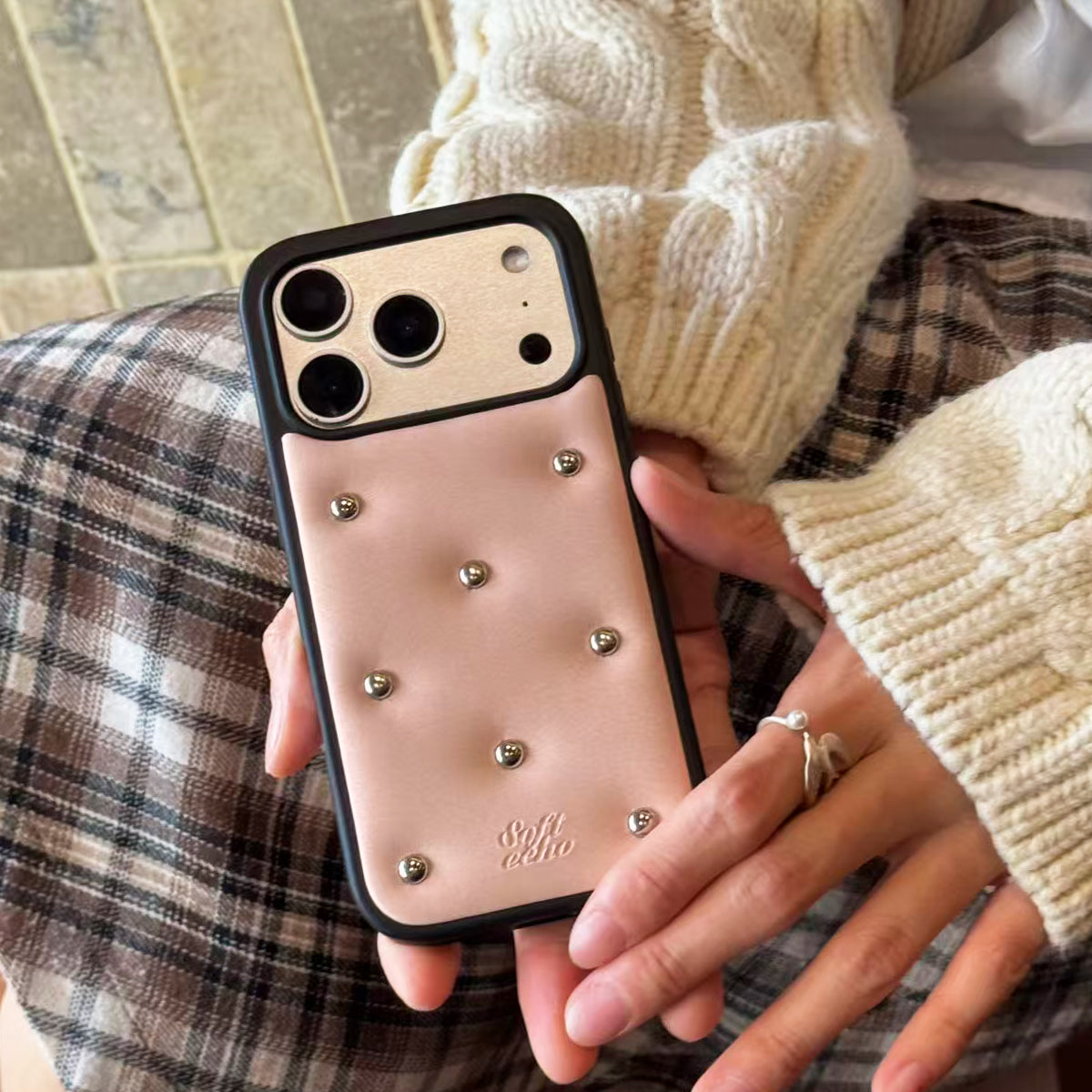 Person holding a phone with a pink case featuring studs
