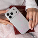 Person holding a silver phone case with pink floral patterns on a textured surface