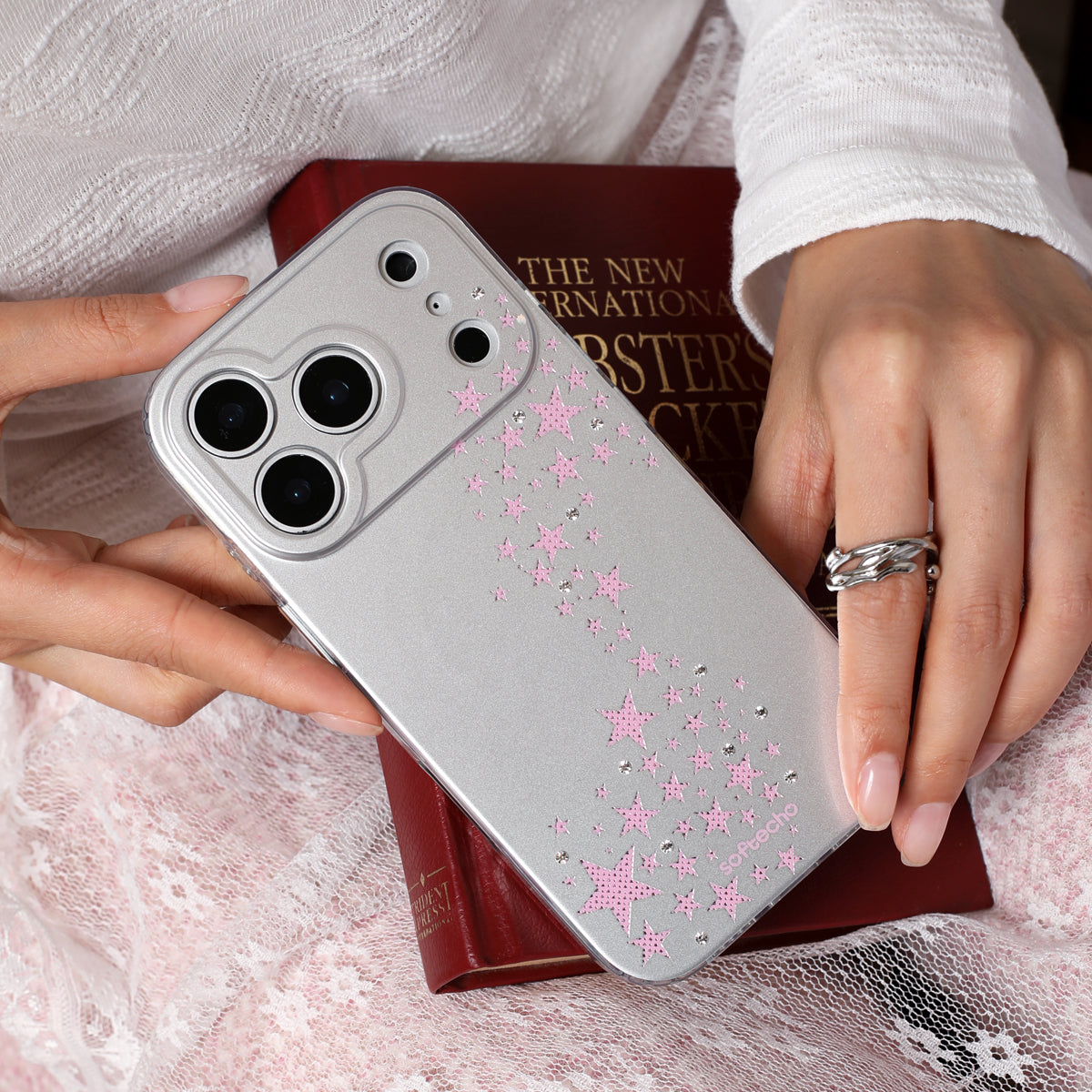 Person holding a silver phone case with pink floral patterns on a textured surface