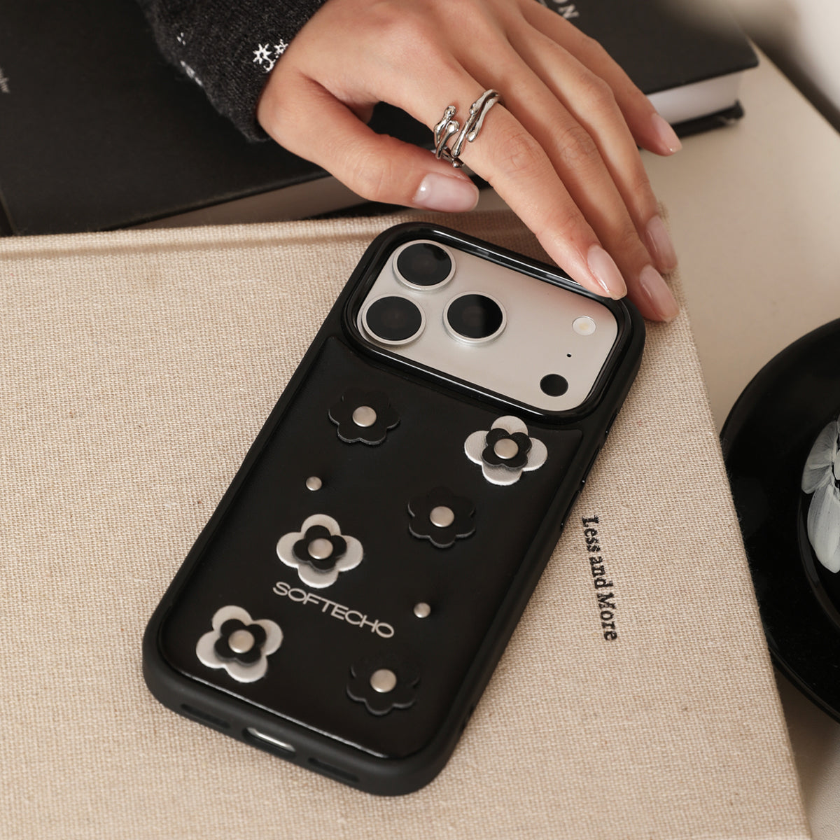Black phone case with floral designs held by a hand on a beige surface