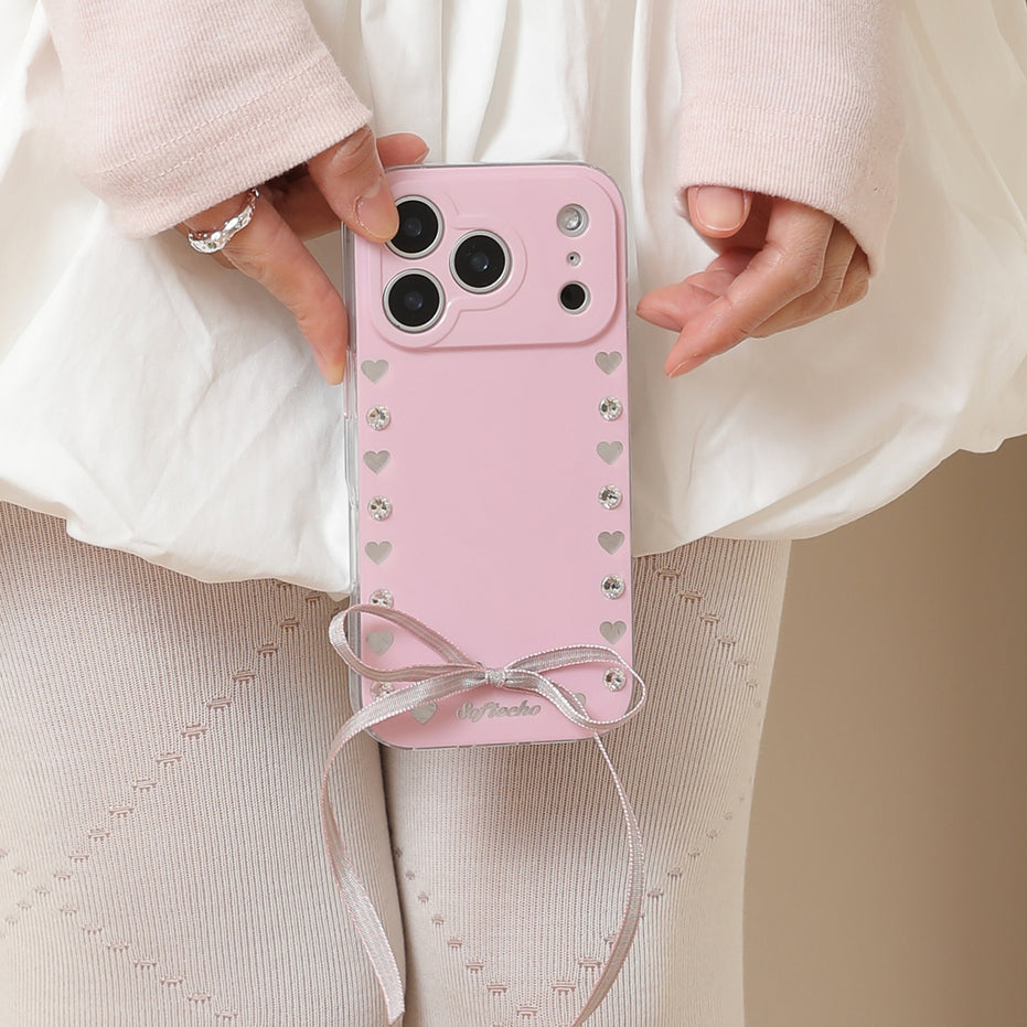 Pink phone case with heart patterns and a bow held by a person wearing a white outfit.