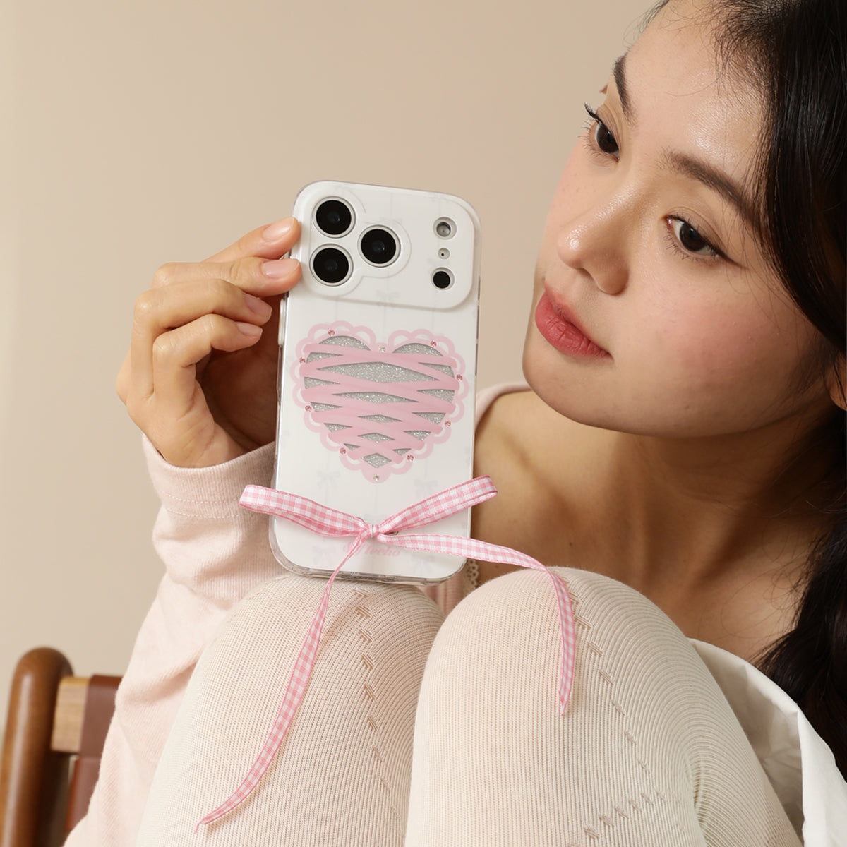 Woman holding a phone with a heart-shaped case and pink ribbon