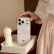 Person holding a phone with a floral case next to a candle on a wooden surface