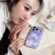 Woman holding a phone with a purple floral case on a light surface.