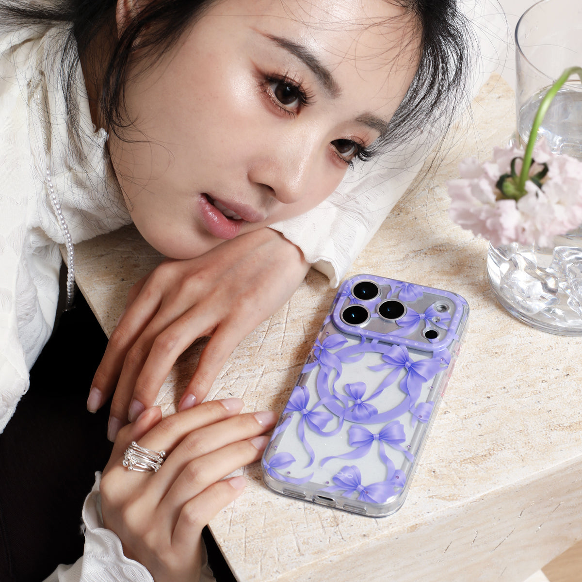 Woman holding a phone with a purple floral case on a light surface.