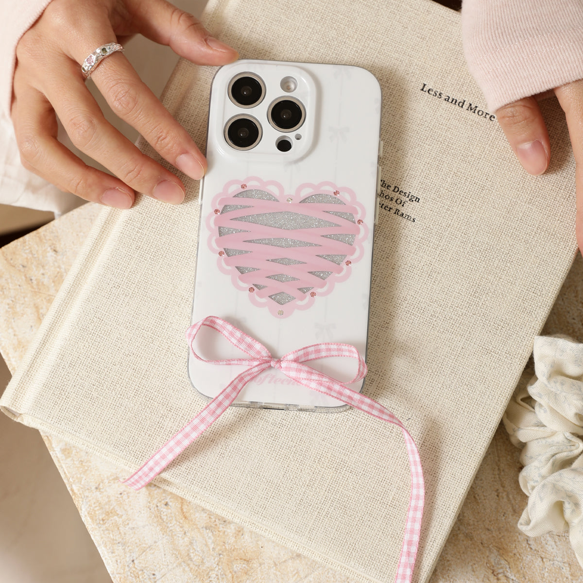 Phone case with pink heart and bow design held by a person on a textured surface.