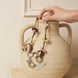 Necklace with heart and leaf charms draped over a ceramic vase